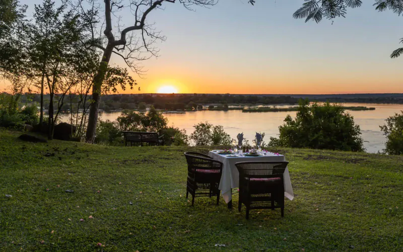 Romantic candlelit dinner table set on grassy overlook with sunset over river, Livingstone Zambia