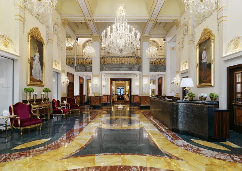 Grand lobby of Hotel Imperial Vienna with chandeliers, ornate walls, red armchairs, and marble floors