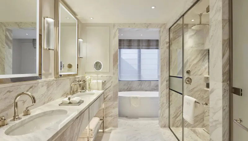 Luxurious beige marble bathroom at Carlton Tower Jumeirah Hotel with double sinks, freestanding tub, and glass shower.
