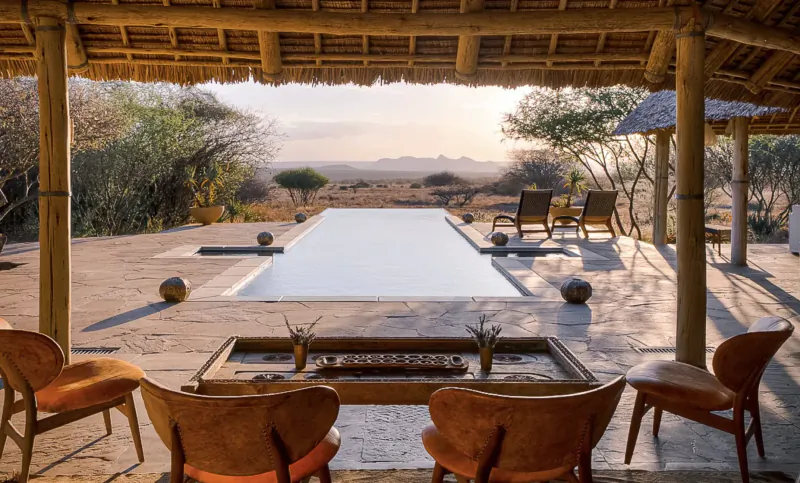 Infinity pool at Tumaren Camp with lounge chairs and fire pit under thatched veranda, savanna sunset view