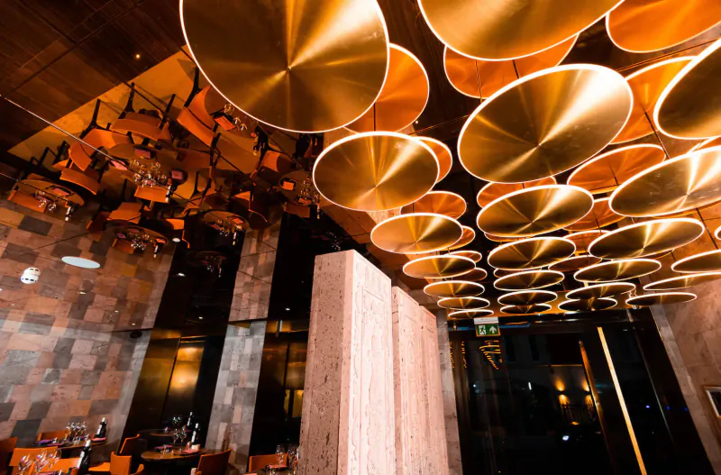 Lusin Mayfair restaurant interior with golden circular ceiling panels, orange chairs, stone walls, and tables.