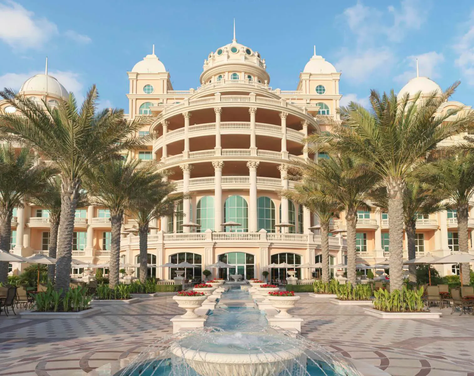 Raffles The Palm Dubai luxury hotel facade with domes, palm trees, and central fountain under blue sky