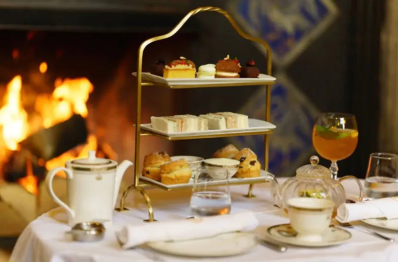 Elegant three-tier stand with cakes, scones, tea set, and drinks by a fireplace at Thornbury Castle.