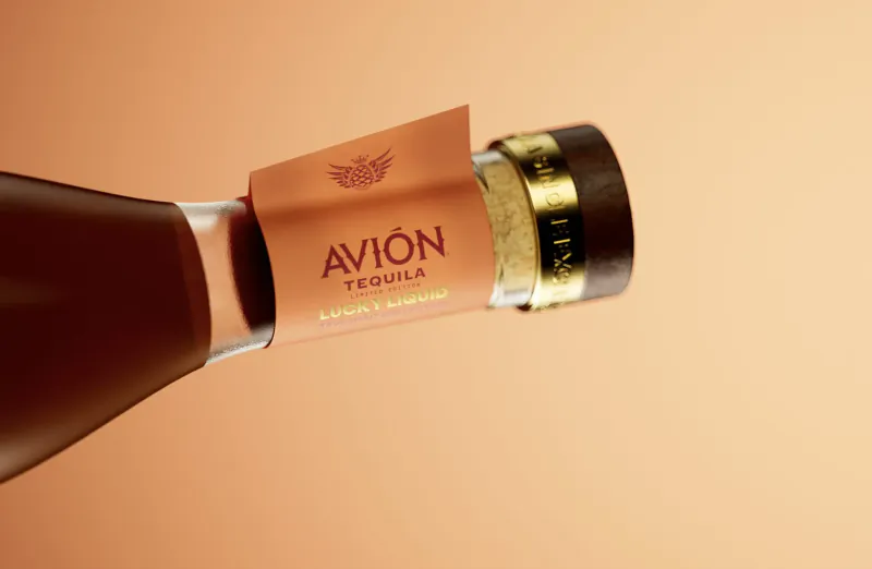 Close-up of Avión Tequila bottle neck with orange label and gold cap on warm background
