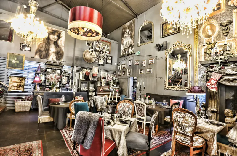 Eclectic interior of Simon’s Restaurant with vintage chairs, tables, chandeliers, large portraits, and ornate decor.