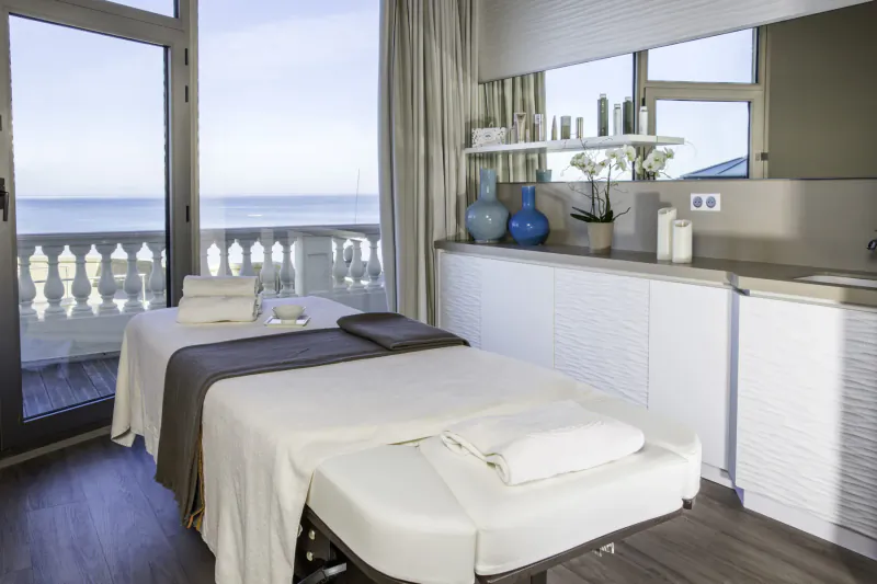 Luxury spa treatment room in Grand Hotel des Thermes with massage table, towels, and sea view balcony.