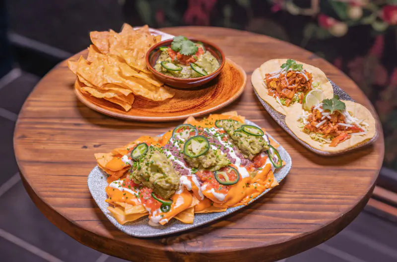 Assortment of Mexican nachos topped with guacamole, salsa, and jalapeños on a wooden table at Mezcalito.