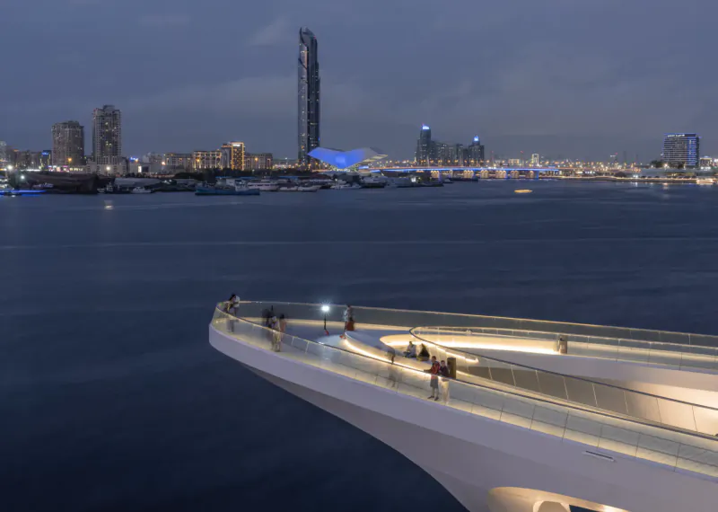 Evening view from curved white pedestrian bridge over river, with people, lit skyscrapers including tall blue tower, and Address Grand Creek Harbour gallery.