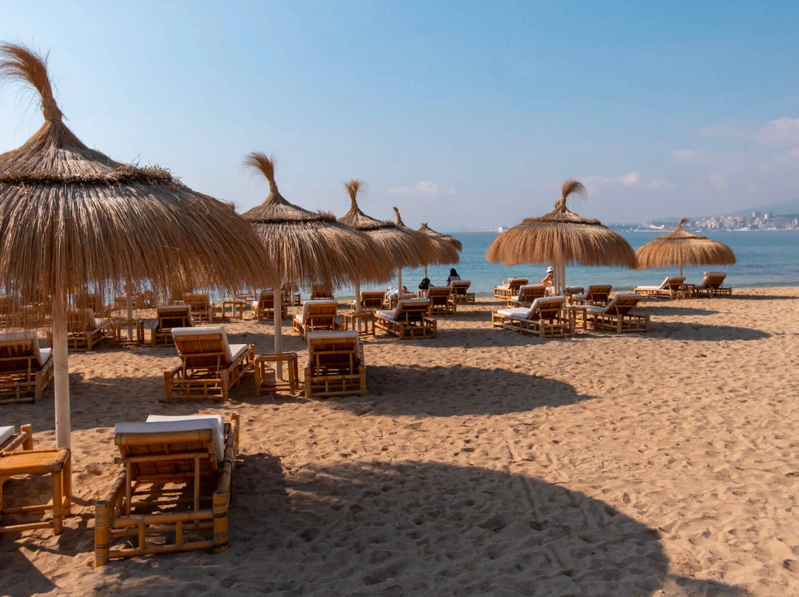Rows of thatched umbrellas and loungers on sandy beach at Gastro Beach in Palma, with sea and city in background