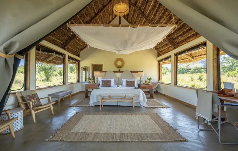 Spacious luxury tent interior at El Karama Lodge, Kenya, with king bed, chairs, and savanna views through large windows.