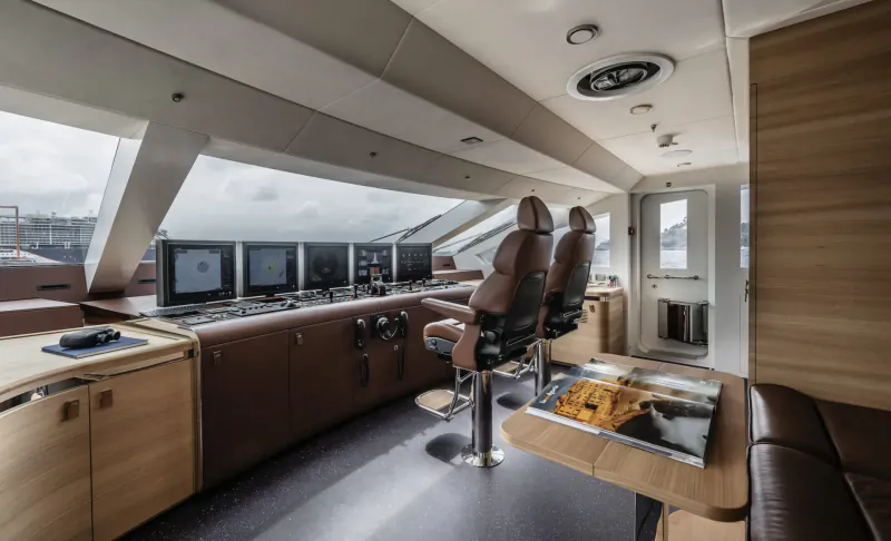 Luxurious yacht bridge with leather captain's chairs, multiple screens, wooden panels, and panoramic sea windows.