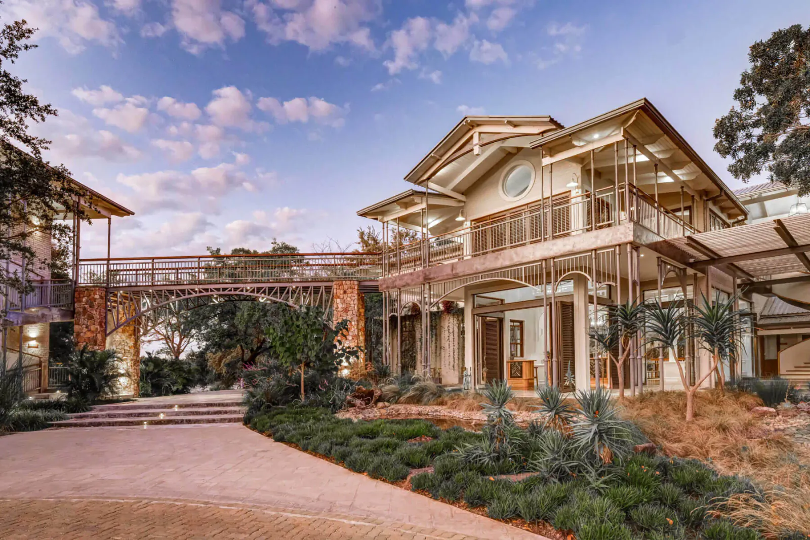 Palm River Hotel: modern multi-level building with connecting bridge, lush gardens, palm trees, and sunset sky near Victoria Falls