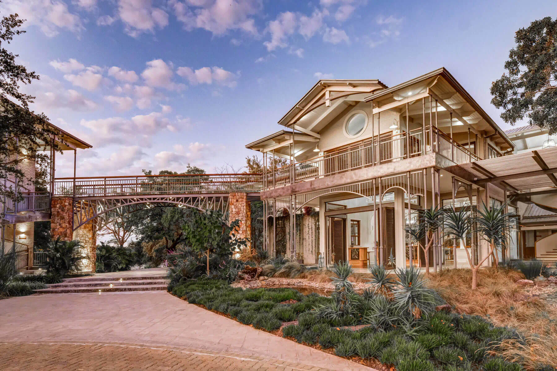 Palm River Hotel: modern multi-level building with connecting bridge, lush gardens, palm trees, and sunset sky near Victoria Falls