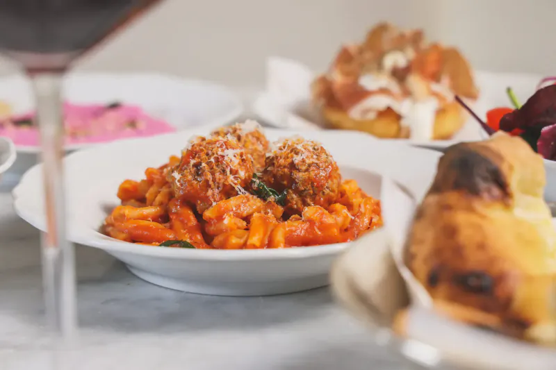 Plate of rigatoni pasta with tomato sauce and meatballs, beside bread and red wine at Italian restaurant.