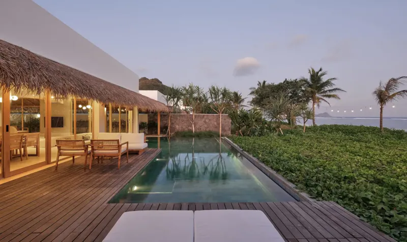 Luxury beachfront villa at Amber Lombok Resort with infinity pool, lounge chairs, tropical garden, and ocean sunset view.