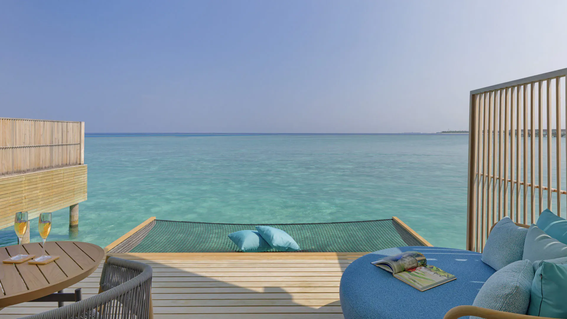 Luxury overwater villa deck at Maldives resort with turquoise ocean view, blue cushions, cocktails on wood table