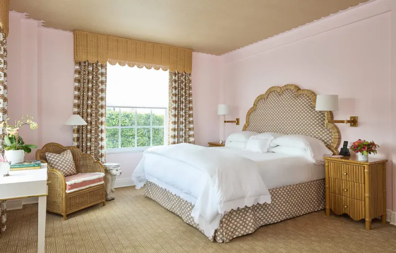 Elegant pink bedroom in Palm Beaches with rattan headboard, white bed, orchids, and window view.