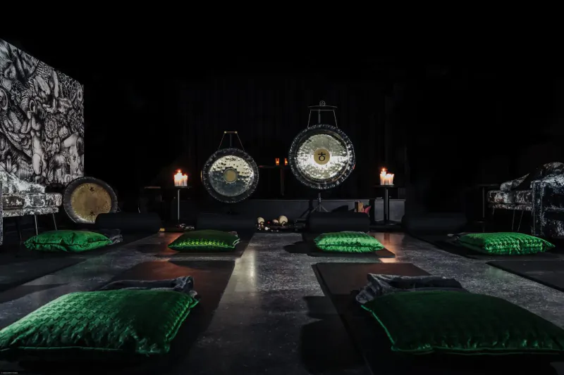 Dark gallery with large gongs, green cushions on mats, candles, and abstract art walls at The Mandrake