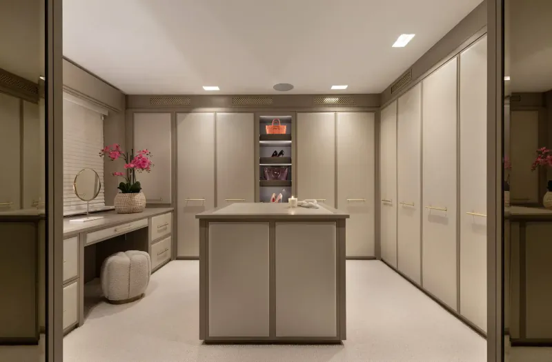 Elegant walk-in closet with beige wardrobes, central island, vanity, orchids, and shoes on shelves.