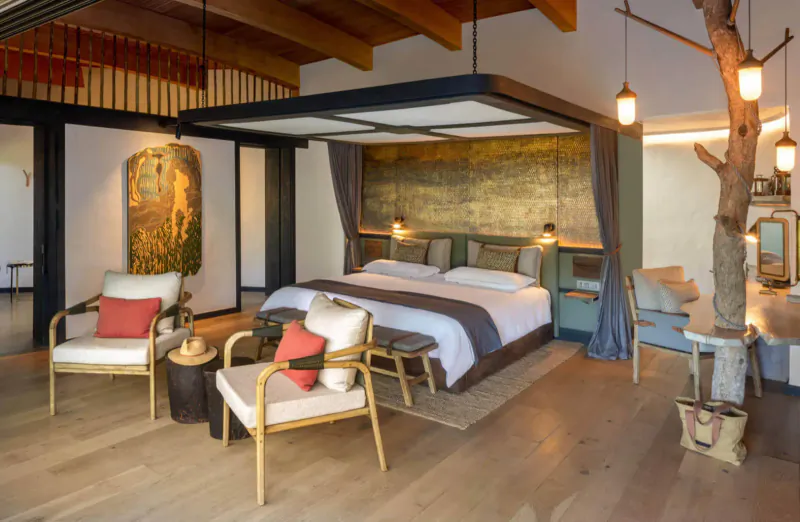Luxurious eco-lodge bedroom in Mashatu Euphorbia with king bed, rattan chairs, gold art, tree trunk, and warm lighting.