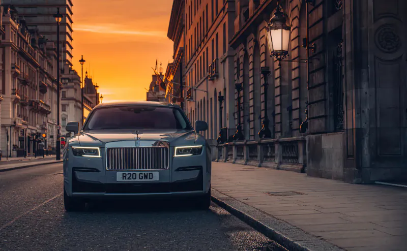 Silver Rolls-Royce with 'ROC 1' plate parked on London street at sunset, historic buildings and lamps.