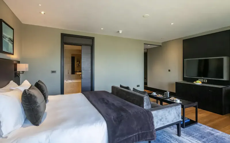 Luxurious hotel bedroom with king bed, gray headboard, TV, side tables, and en-suite bathroom door at Twr y Felin.