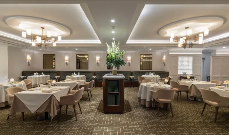 Elegant spa restaurant at Carden Park with white tablecloths, upholstered chairs, large floral centerpiece, and ambient lighting.