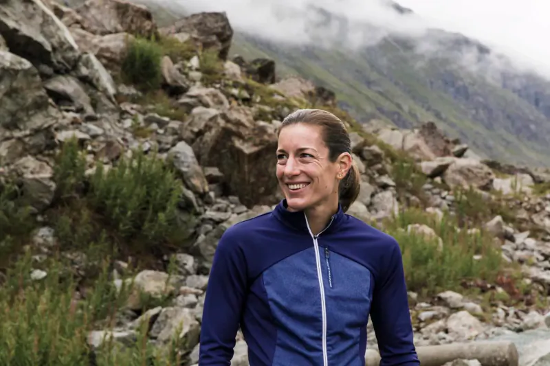 Smiling female triathlete Nicola in blue jacket amid rocky mountain stream and mist