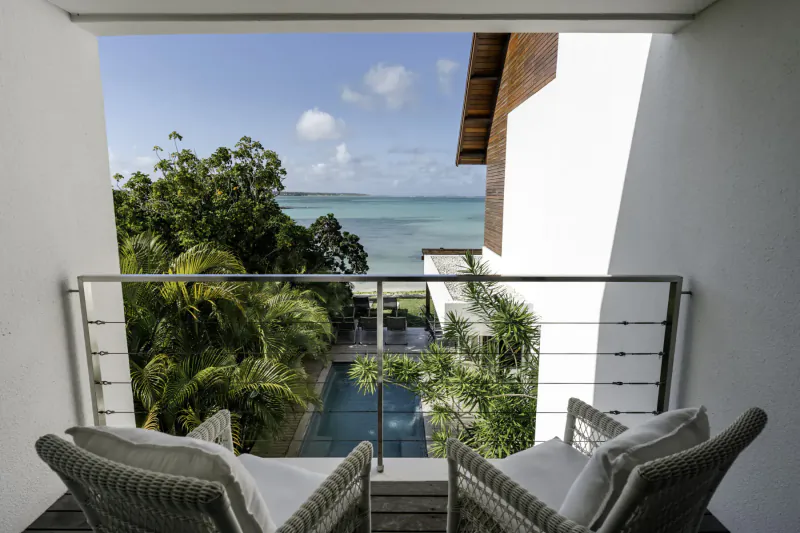View from Villa Sapphire balcony: white lounge chairs, infinity pool, tropical trees, turquoise ocean, Belle Mare beach.