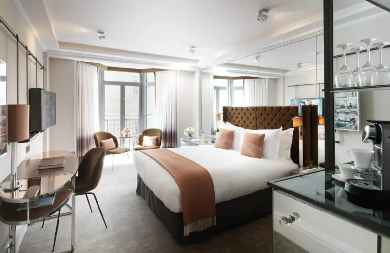 Elegant hotel suite at The Athenaeum with king bed, armchairs, desk, coffee station, and city view balcony.