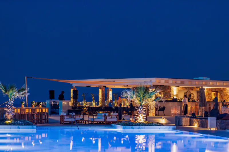Nighttime poolside bar at Abaton Island Resort & Spa with lit palm trees, lounge seating, and blue pool reflections.