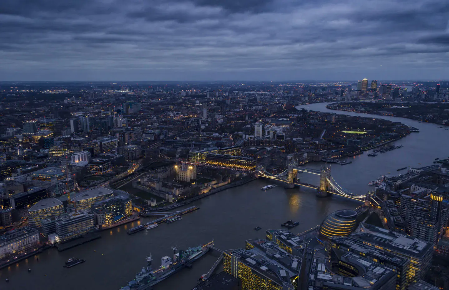 Aerial view of Tower Bridge illuminated at dusk over the River Thames in London skyline.