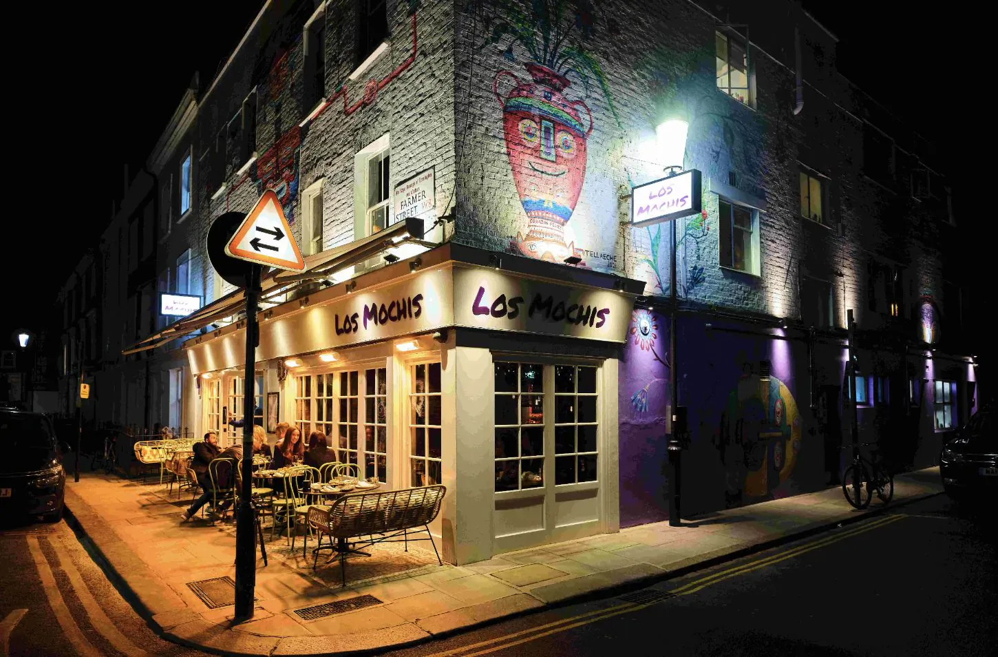 Los Mochis restaurant in Notting Hill at night, with Mexican-Japanese fusion signage, vibrant mural, outdoor seating, and street lamps.