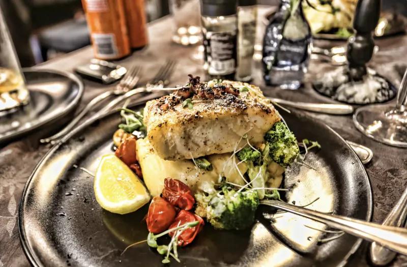 Grilled white fish fillet on mashed potatoes with broccoli, roasted tomatoes, lemon wedge on elegant plate at Simon’s Restaurant