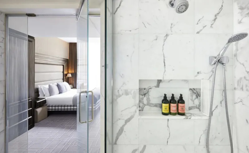 Eccleston Square Hotel luxury suite: king bed through glass door, marble shower with shampoo bottles in niche