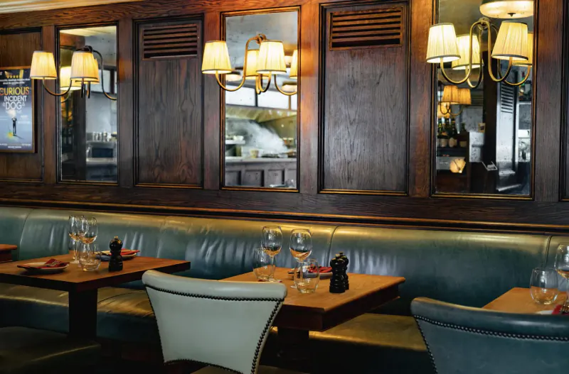 Elegant Italian steakhouse interior with wooden paneled walls, brass lamps, teal leather booths, and tables set with wine glasses and pepper mills.