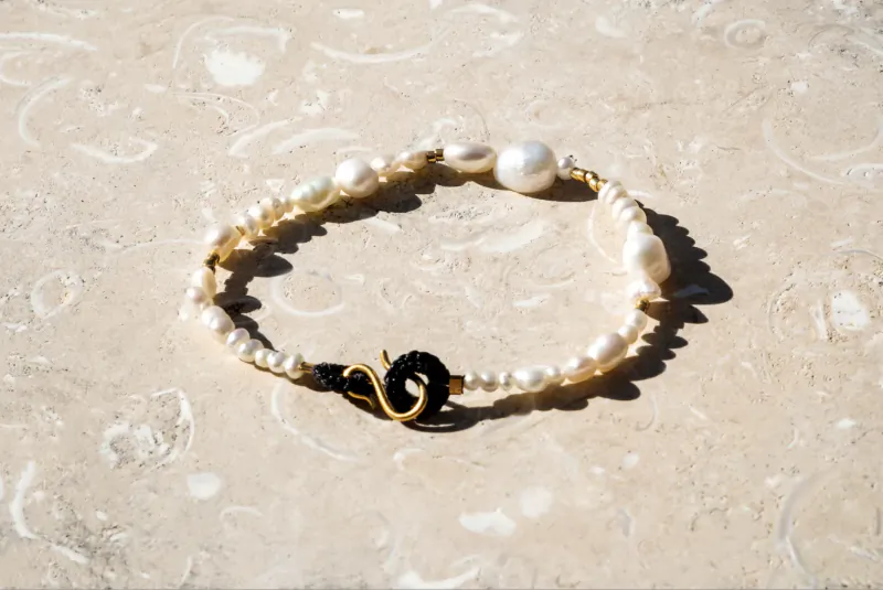 Pebble & Loop pearl bracelet with black snake loop clasp on stone surface