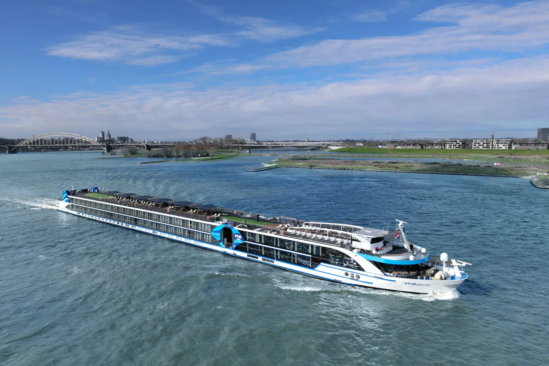 VIVA ENJOY cruise ship sailing on river near bridges and industrial skyline under blue sky