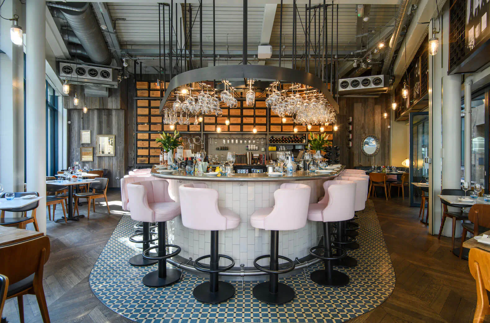 Modern industrial bar with pink stools, hanging glass chandeliers, and tiled floor in Marylebone Village restaurant