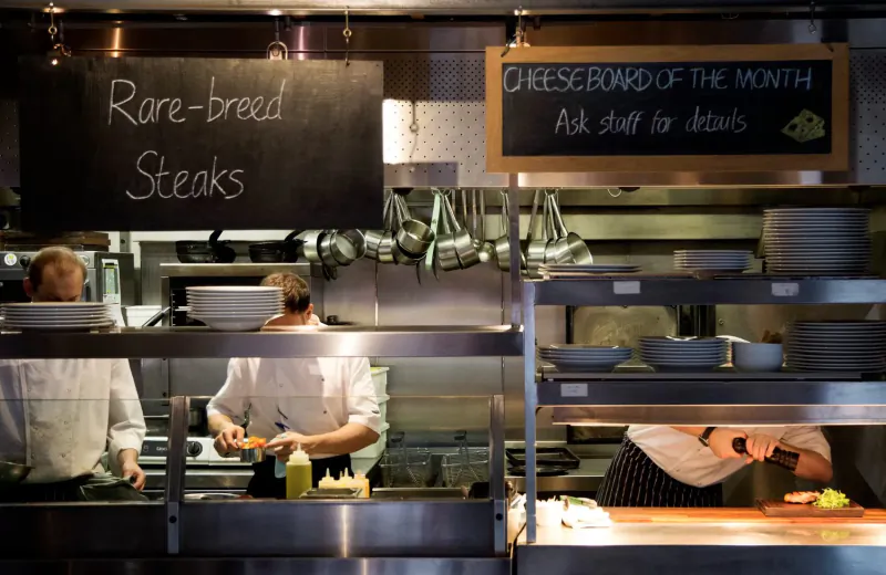 Busy kitchen: chefs preparing rare-breed steaks; signs for 'Rare-breed Steaks' and 'Cheese Board of the Month, ask staff for details'