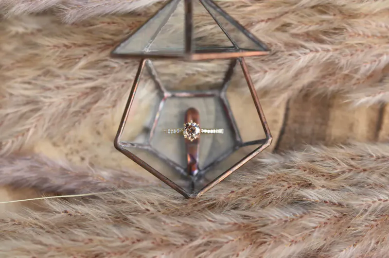 Open geometric glass display case with gold engagement ring on fluffy fur backdrop