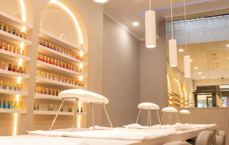 Modern nail salon interior with colorful polish shelves, arched lighting, white manicure stations, and chairs in chic setting