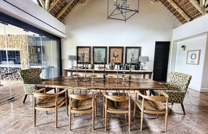 Spacious dining room in Monwana Game Lodge with long wooden table, chairs, artwork, chandelier, and thatched ceiling.