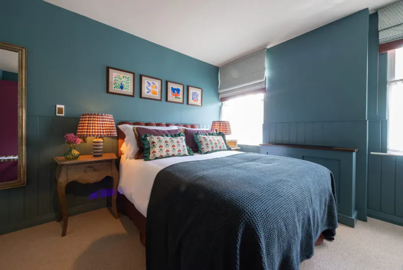 Cozy teal bedroom with king bed, patterned pillows, lamps, flowers, and colorful wall art in George & Dragon Marlow.