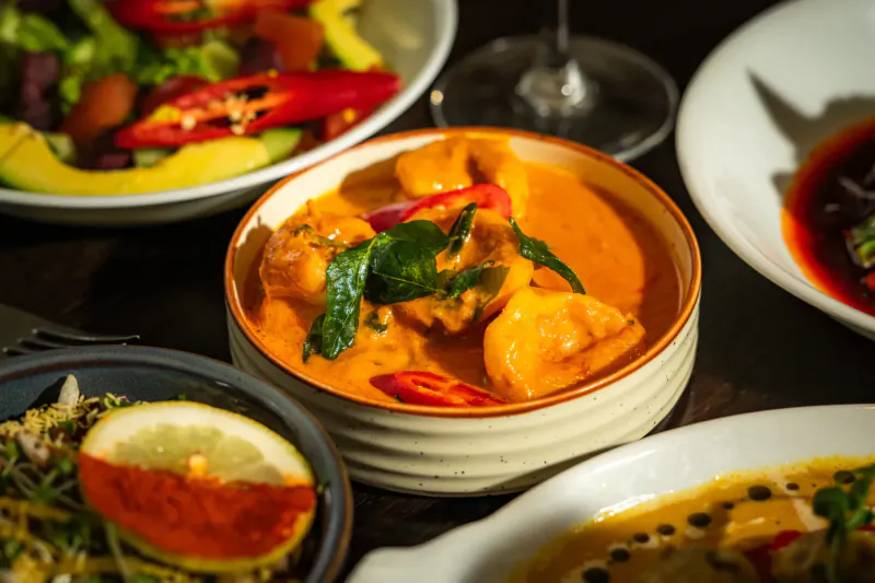 Assortment of Indian dishes including red curry with prawns and chilies, salads, and cocktails at Mint Leaf London