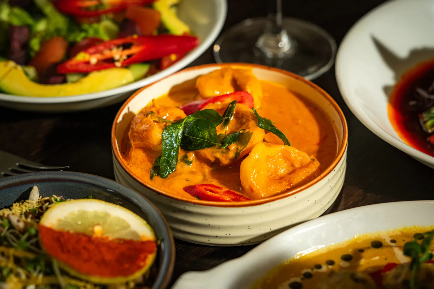 Assortment of Indian dishes including red curry with prawns and chilies, salads, and cocktails at Mint Leaf London
