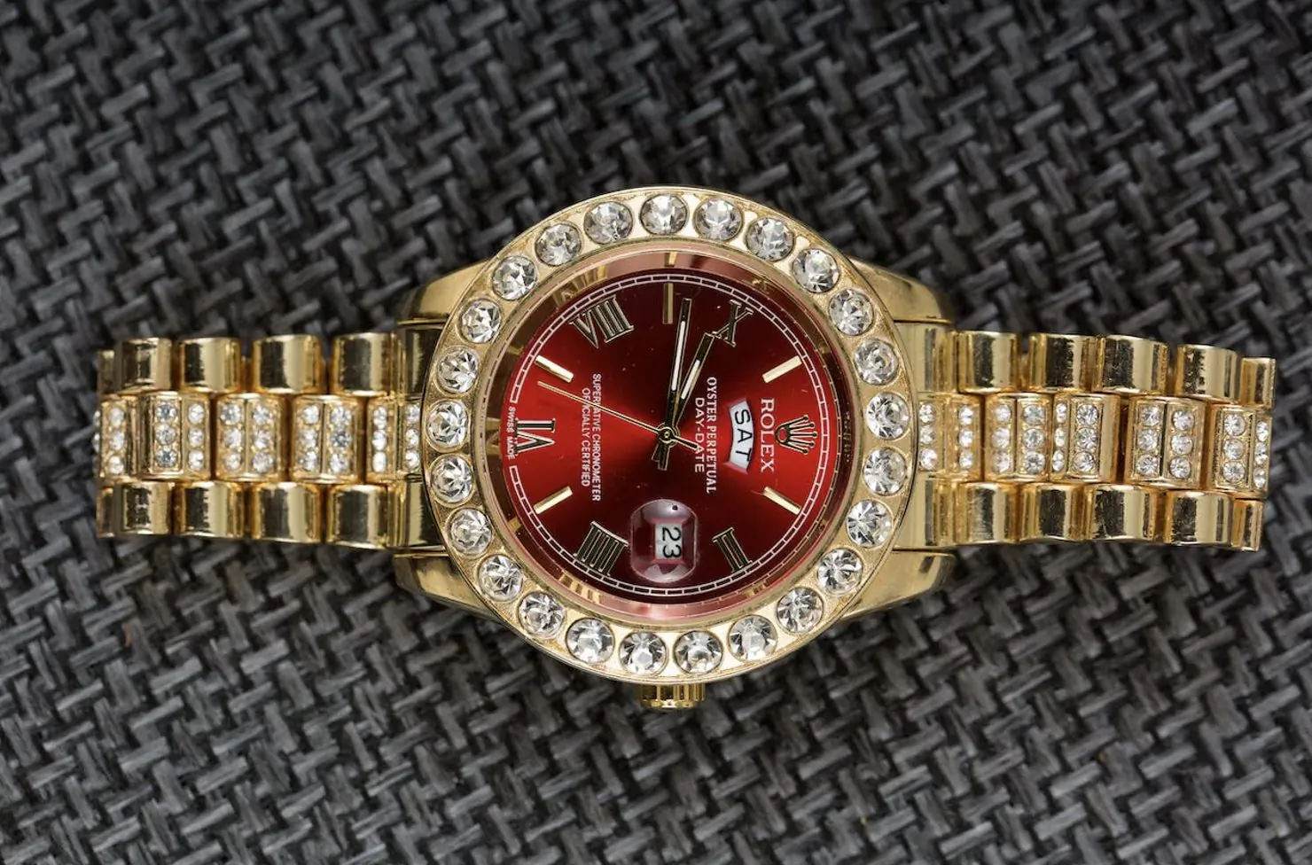 Luxurious gold Rolex-style watch with red dial, Roman numerals, date window, diamond bezel on gold bracelet