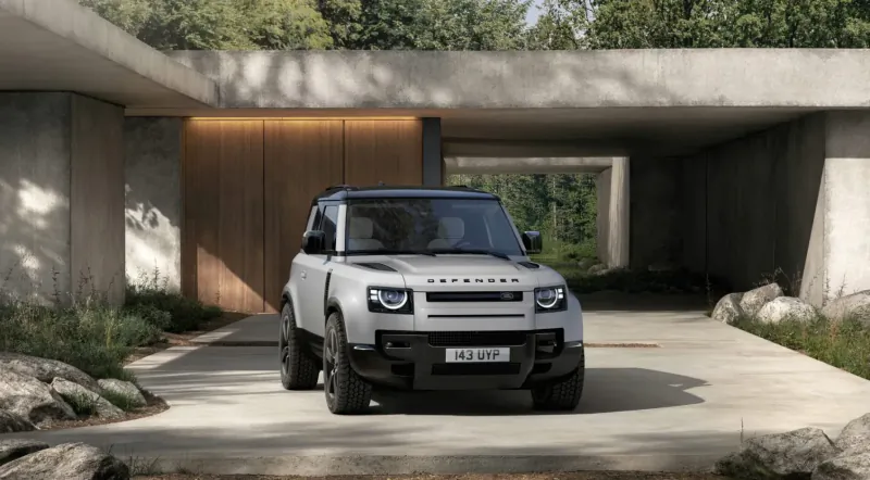 White Land Rover Defender parked in modern outdoor garage with concrete architecture and greenery.