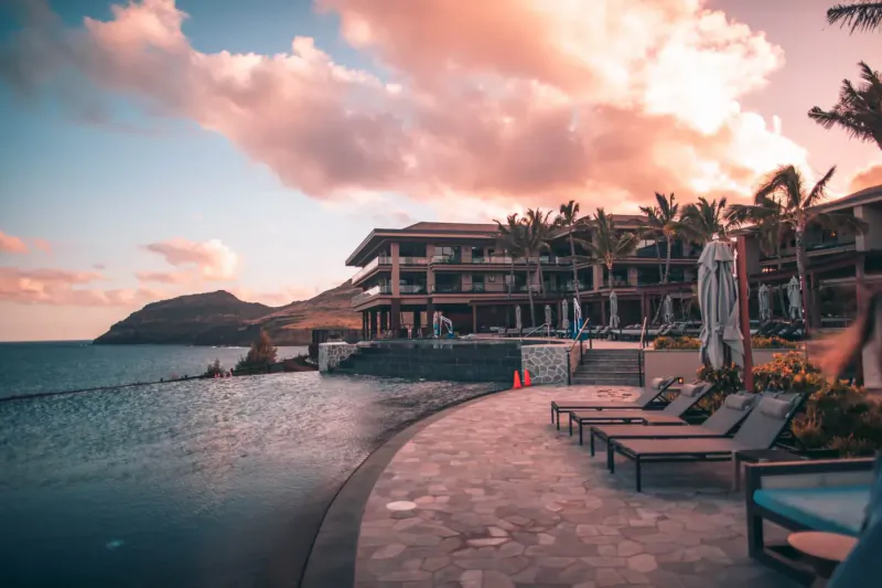 Luxury beachfront resort infinity pool at sunset with lounge chairs, palms, and ocean view