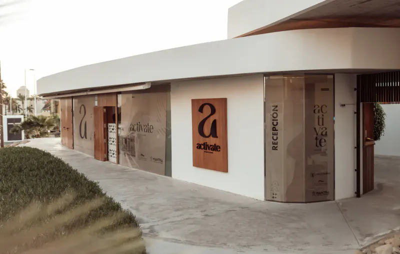 Modern white curved facade of Baobab Suites resort in Tenerife with 'Baobab' and 'Suites' signage, glass doors, and landscaped path.